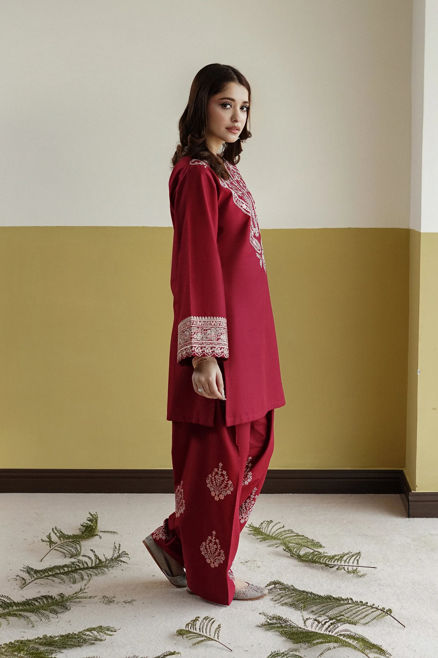 Woman in a red traditional outfit standing against a yellow and white wall with decorative elements on the floor.